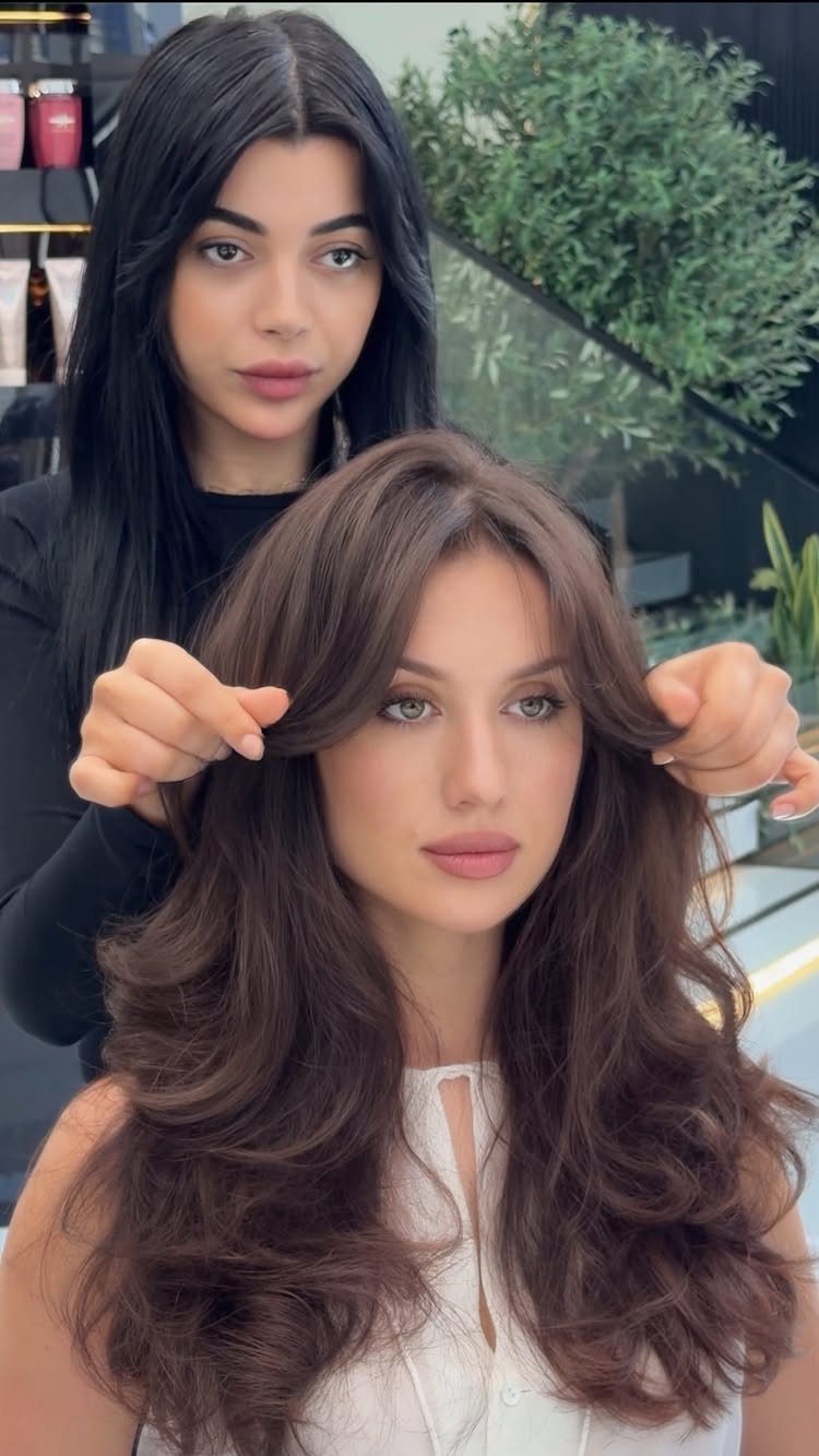 Woman with long brown layers and parted curtain bangs being styled in a salon
