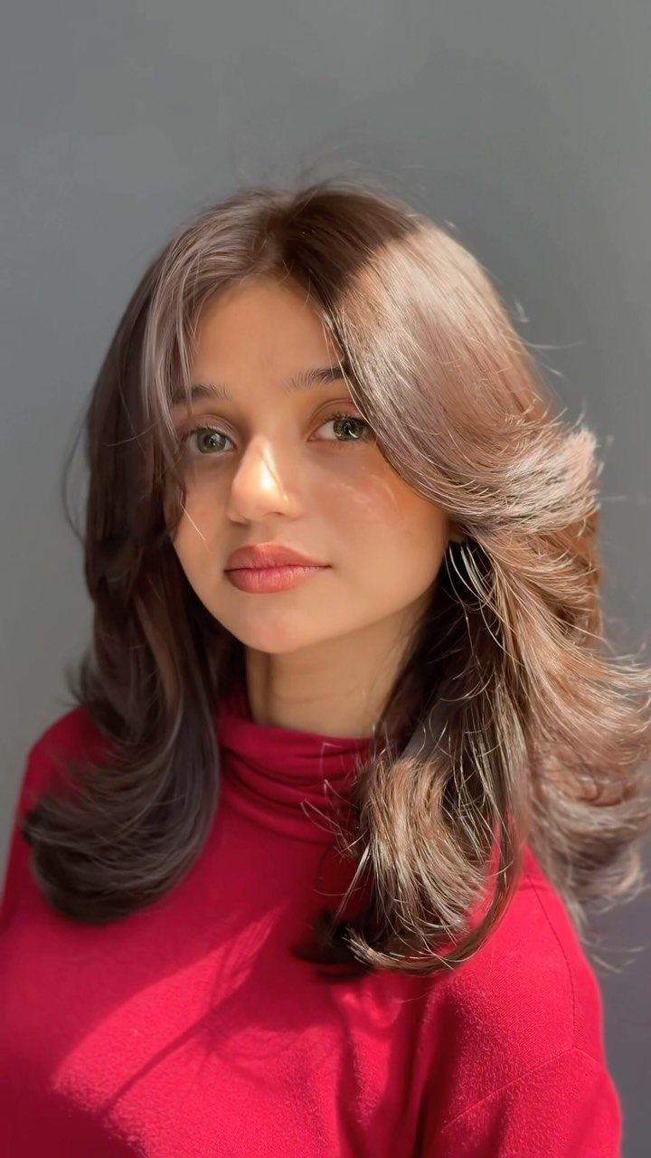 Woman with long brown layers and curled face-framing pieces wearing a red top