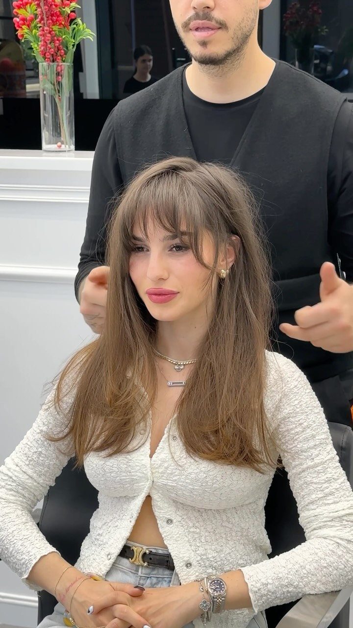 Woman with long layered brown hair and tousled fringe seated in a salon chair