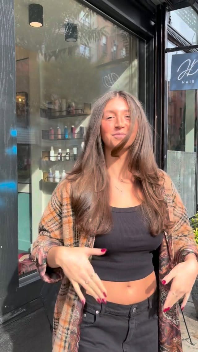 Woman with long brown blended layers standing outside a hair salon
