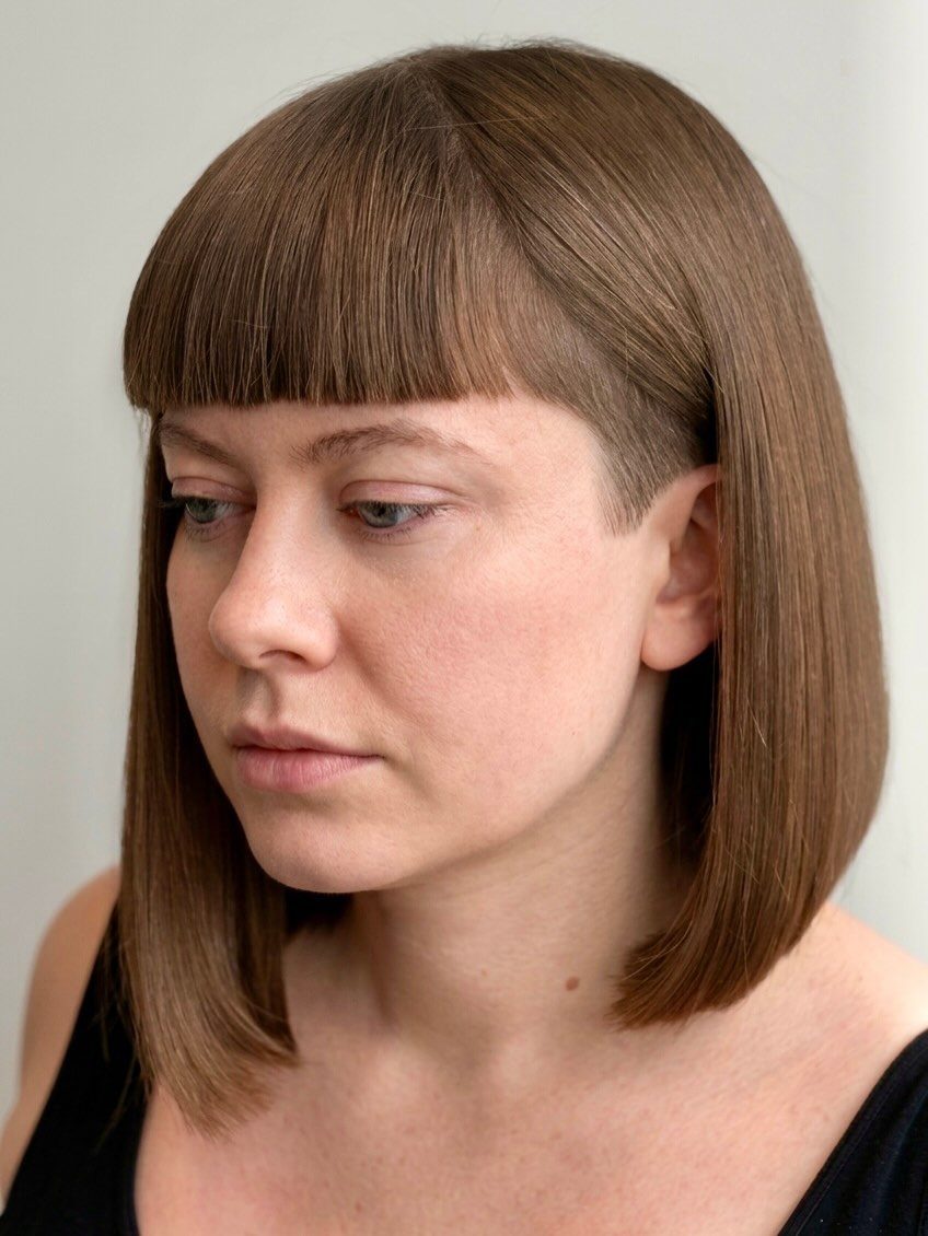 Woman with smooth brown bob and blunt bangs against gray background
