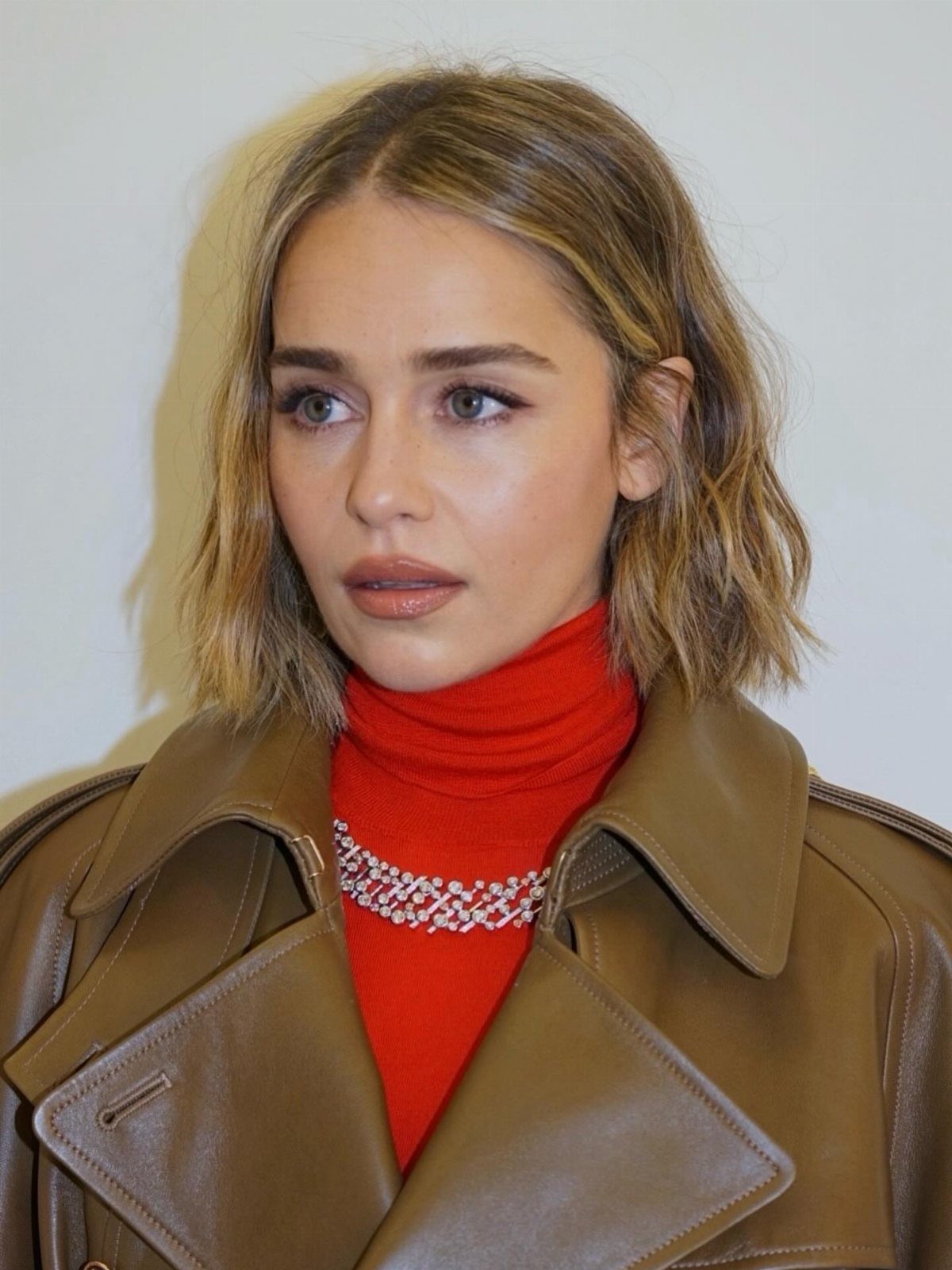 Blonde woman with a softly choppy bob, red top, and brown leather jacket