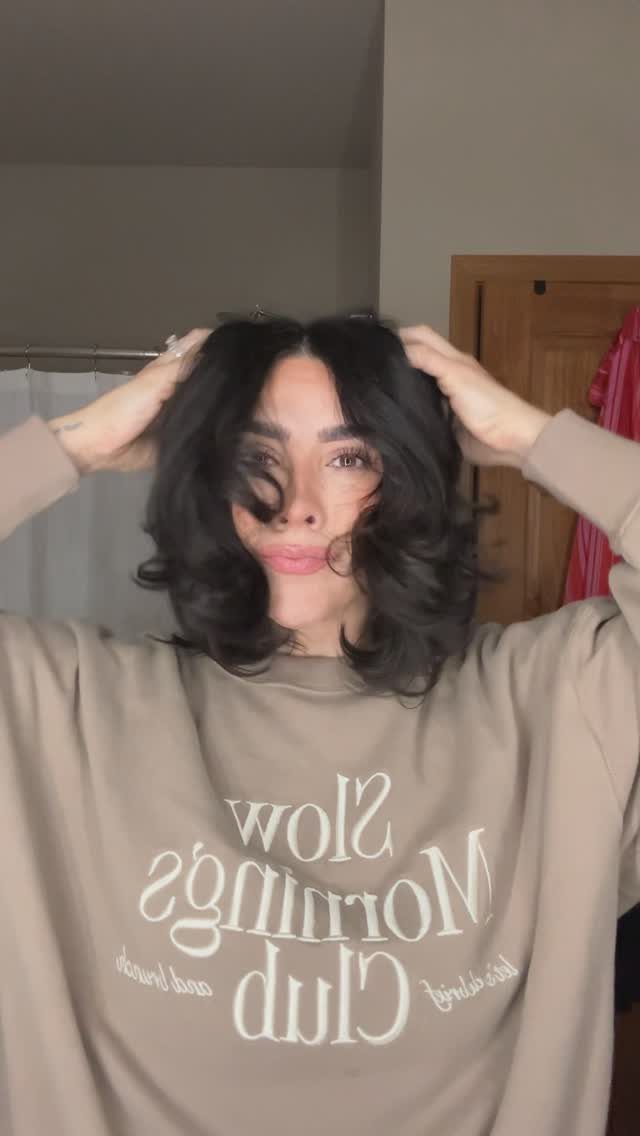 Person showing a voluminous curly lob with face-framing layers indoors