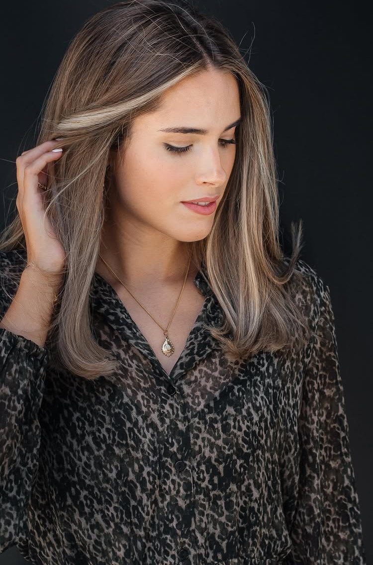 Woman with highlighted layered brown hair touching the face-framing strands