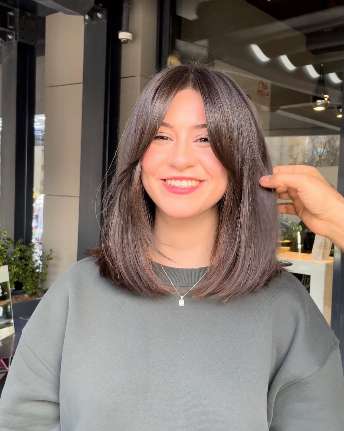 Person wearing a smooth, center-parted shoulder-length dark brown bob in a salon