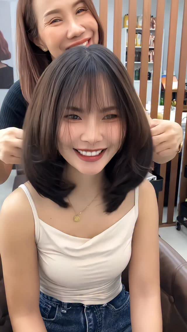 Woman with a shoulder-length dark bob and wispy bangs in a salon chair