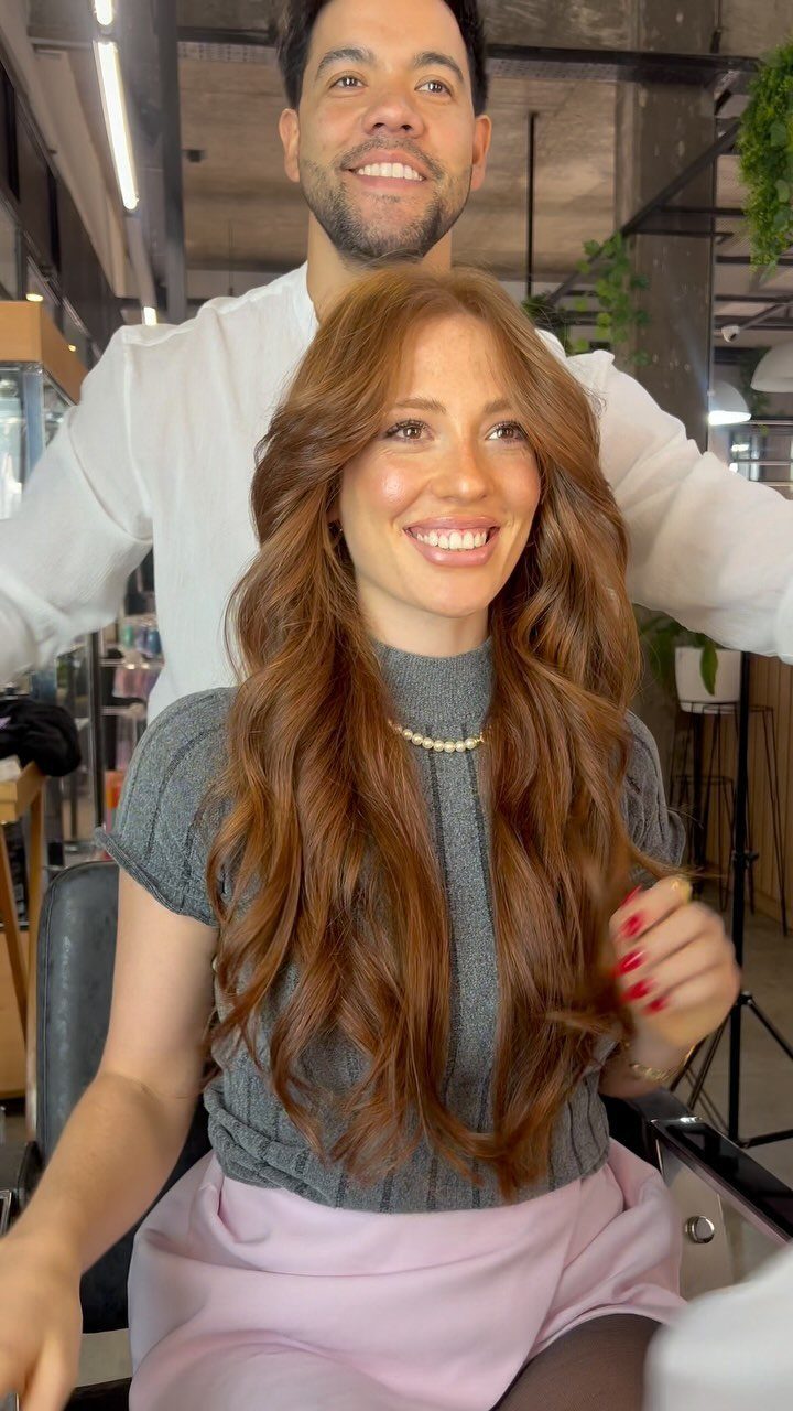 Woman with long wavy auburn hair, fringe, and lighter balayage highlights in a salon