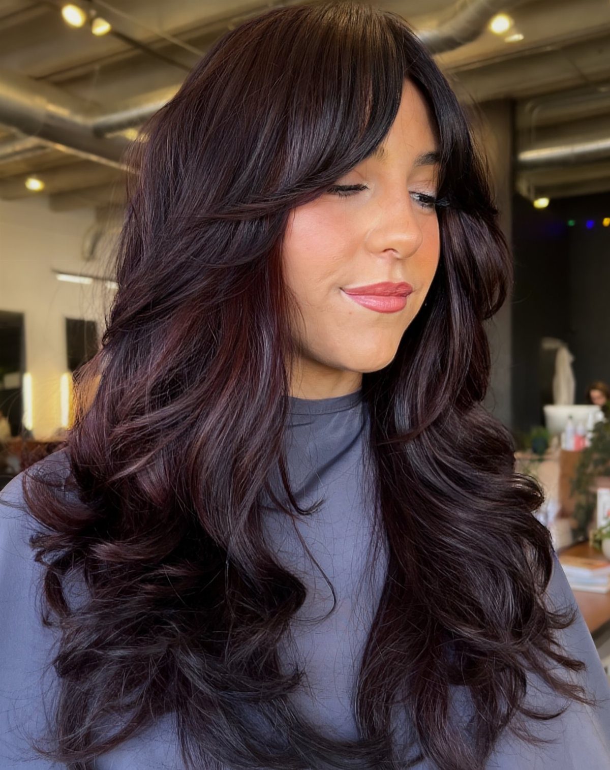 Woman showing voluminous blowout waves with sweeping bangs in a salon