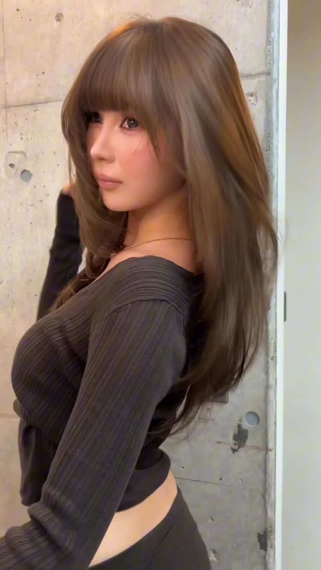 Woman with long brown hair and blunt bangs wearing a dark ribbed top