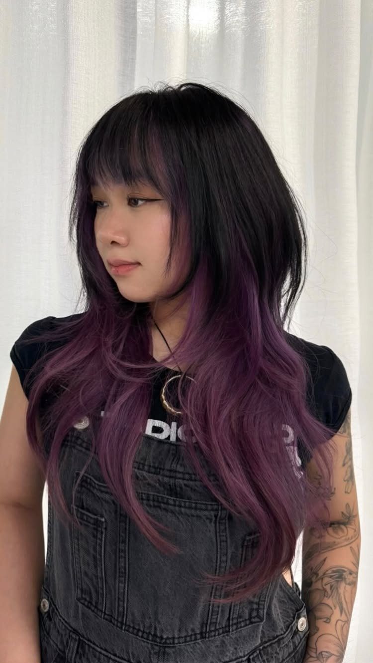 Long purple-tipped hair with a piecey, uneven fringe against white curtains