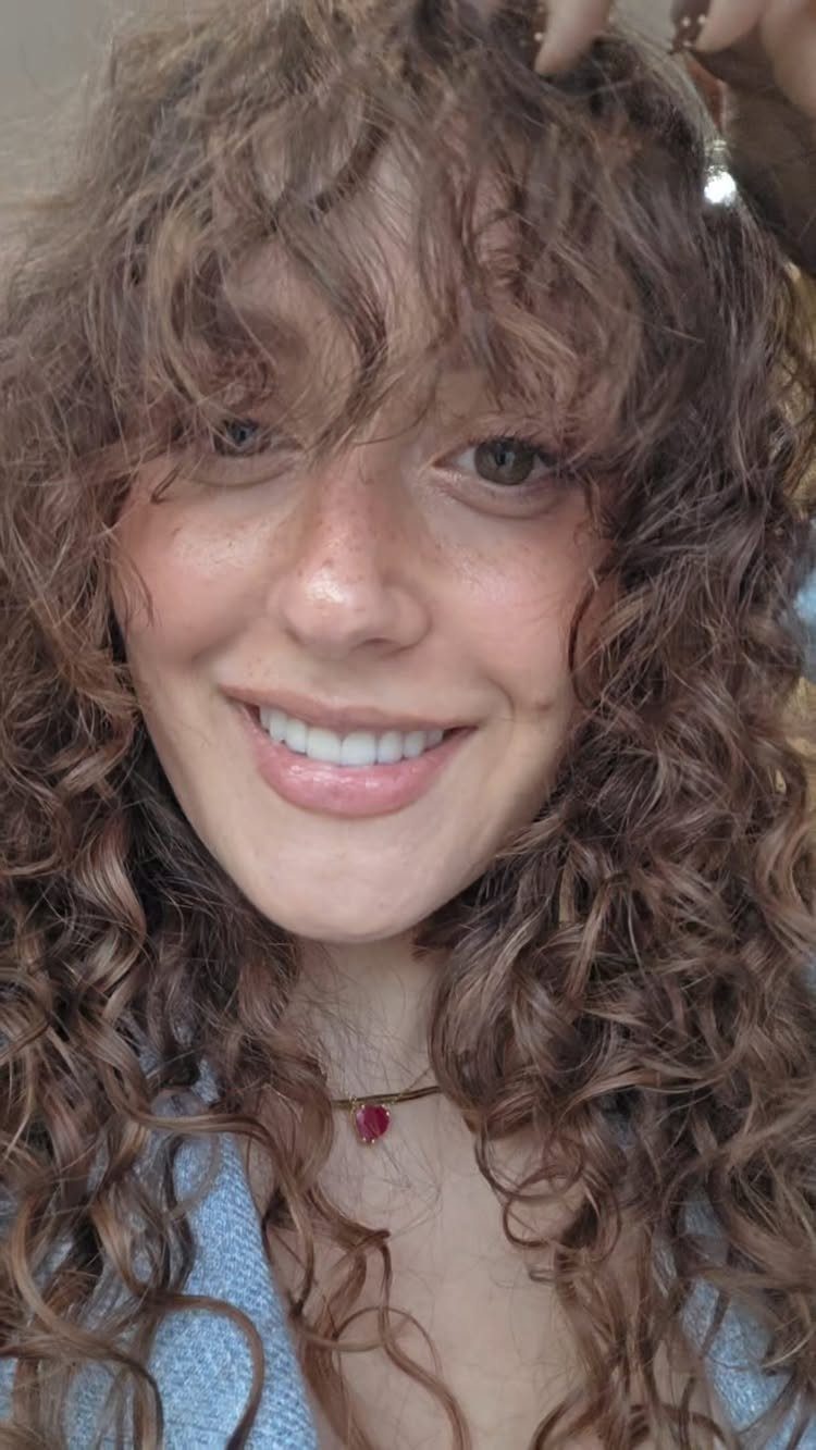 Woman with long brown curls and a curly fringe framing her face