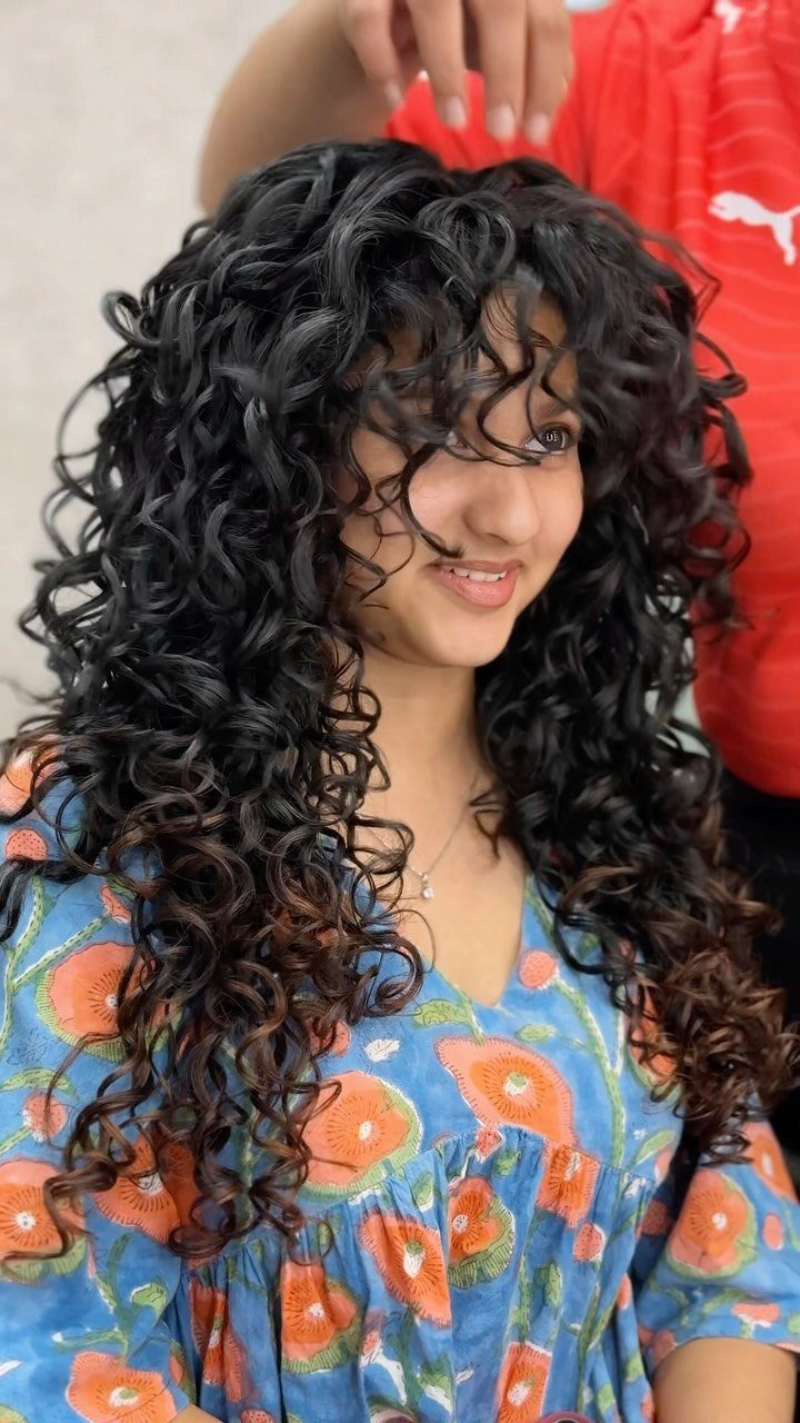 Long black curls frame the face, with curly bangs falling across the forehead