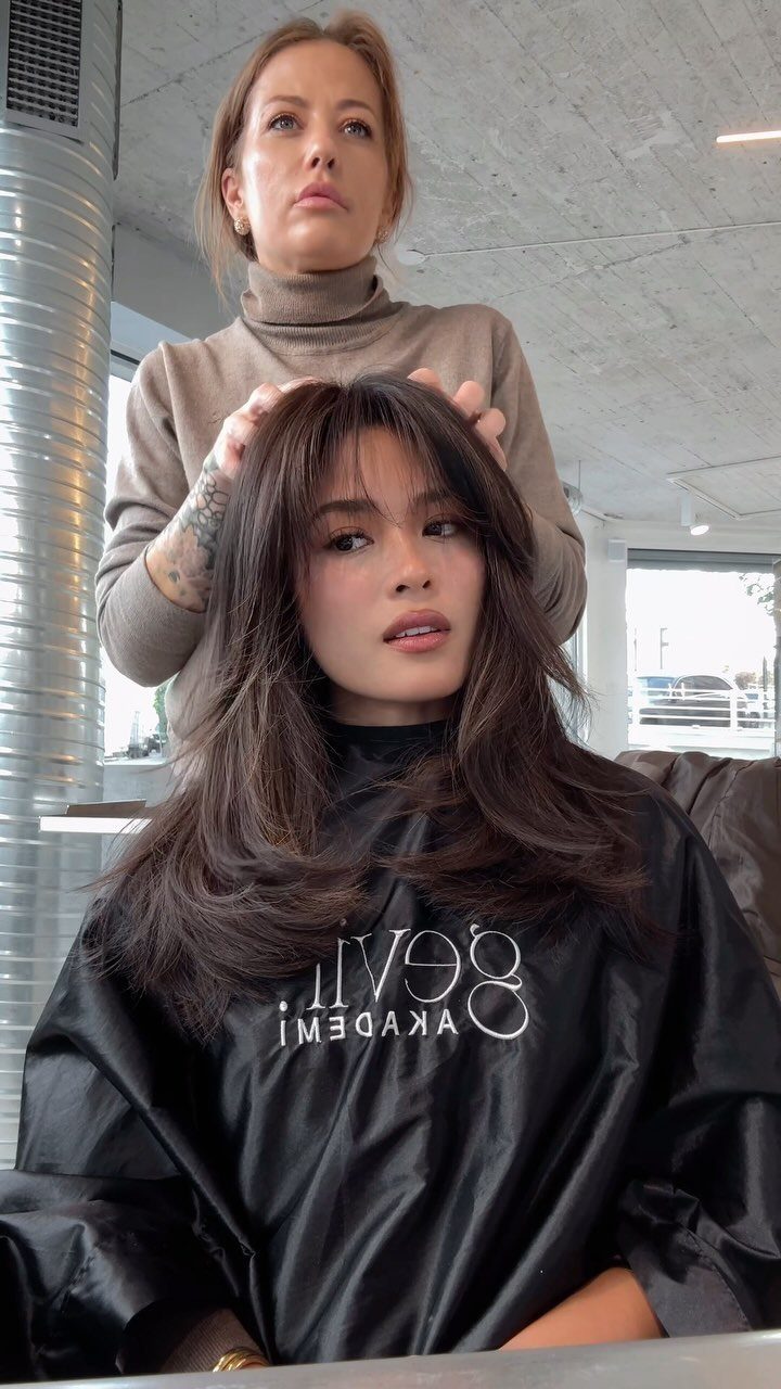 Long dark hair with center-parted curtain bangs styled in a salon chair