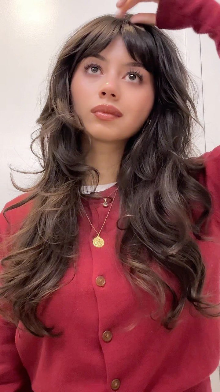 Woman with long dark wavy hair and eyebrow-grazing bangs in a red top