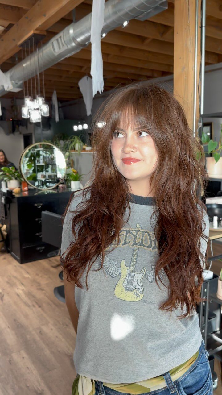 Woman with long, shaggy brown layers and wispy bangs in a salon