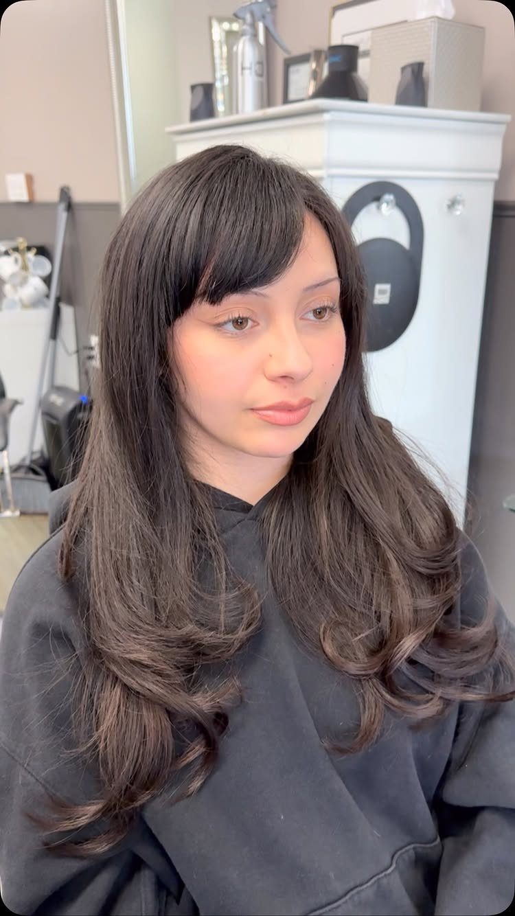 Woman with long dark layered hair and softly curved bangs in a salon