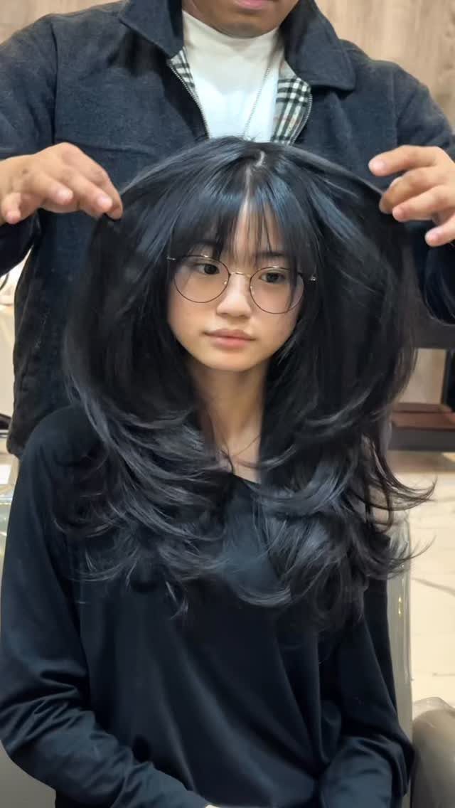 Long black hair with wispy bangs styled in voluminous layers in a salon
