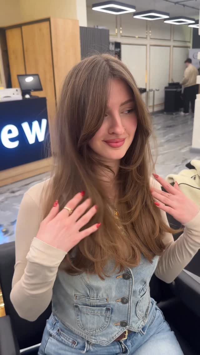 Woman showing long, voluminous layered hair with sweeping face-framing pieces in a salon