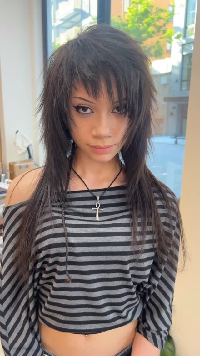 Woman with long dark choppy layers and wispy bangs posing by a window