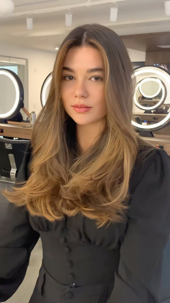 Woman displaying long highlighted layers with curled ends in a bright hair salon