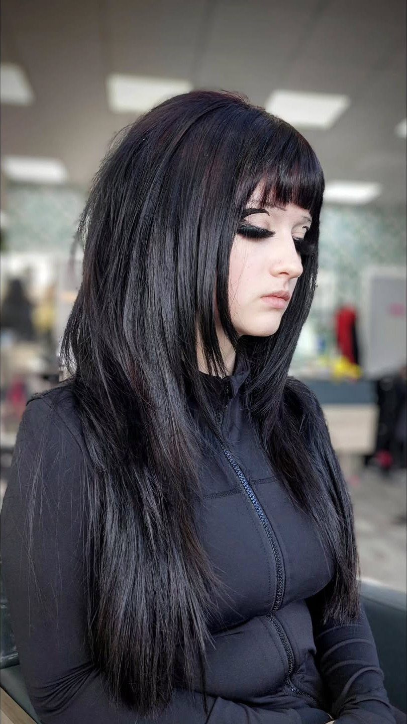 Woman with long straight layered black hair and blunt bangs in a salon