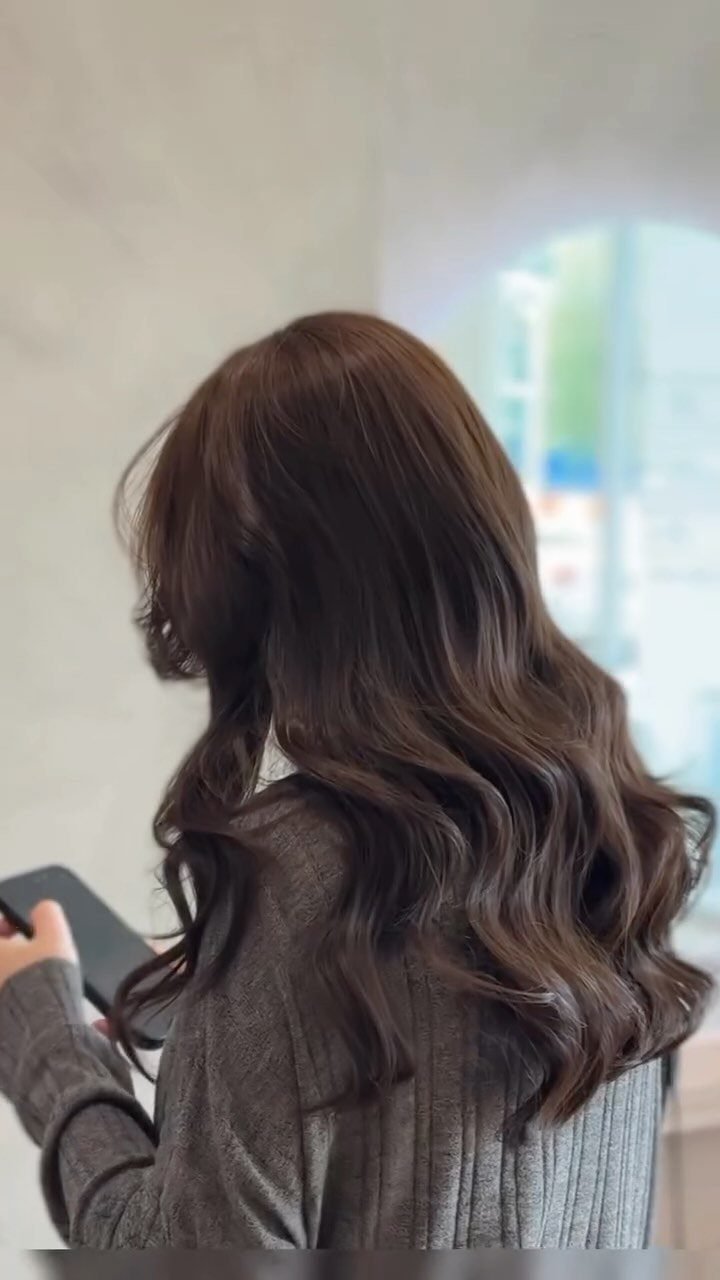 Long dark brown hair styled in soft, layered curls over a gray sweater