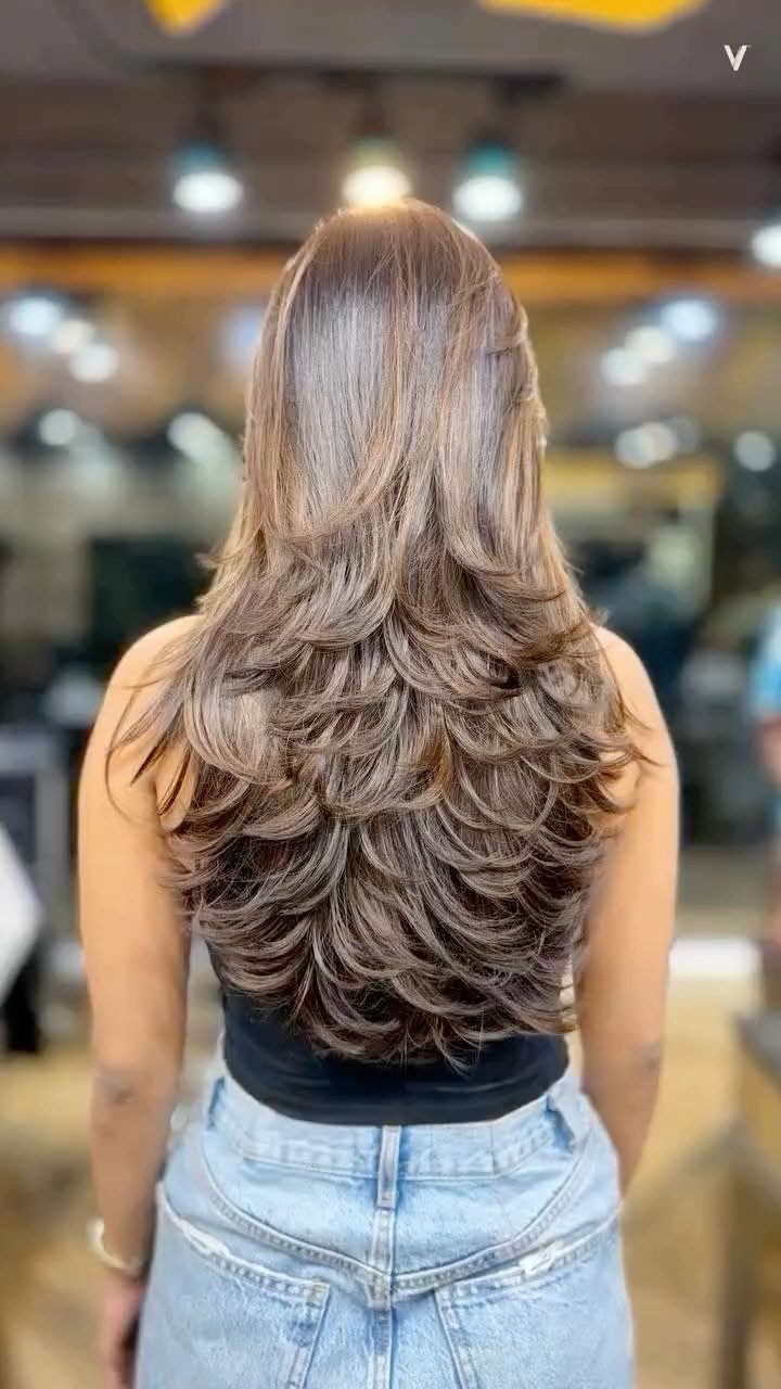 Long brown layered hair cascades in curled ends down a person's back