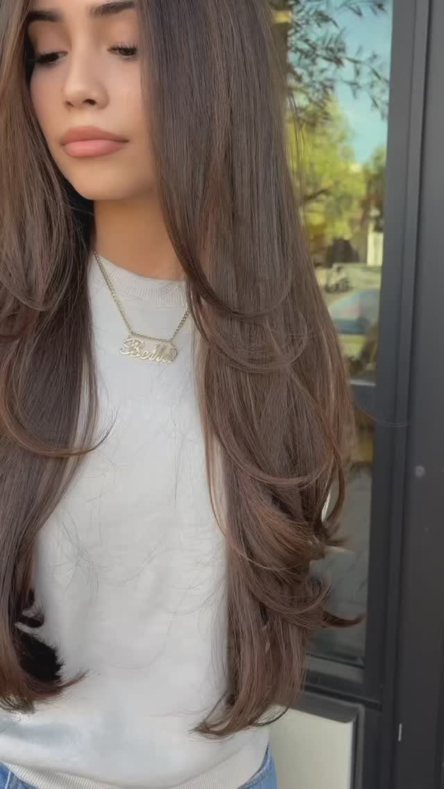 Woman with long brown hair styled in soft cascading layers beside a glass door