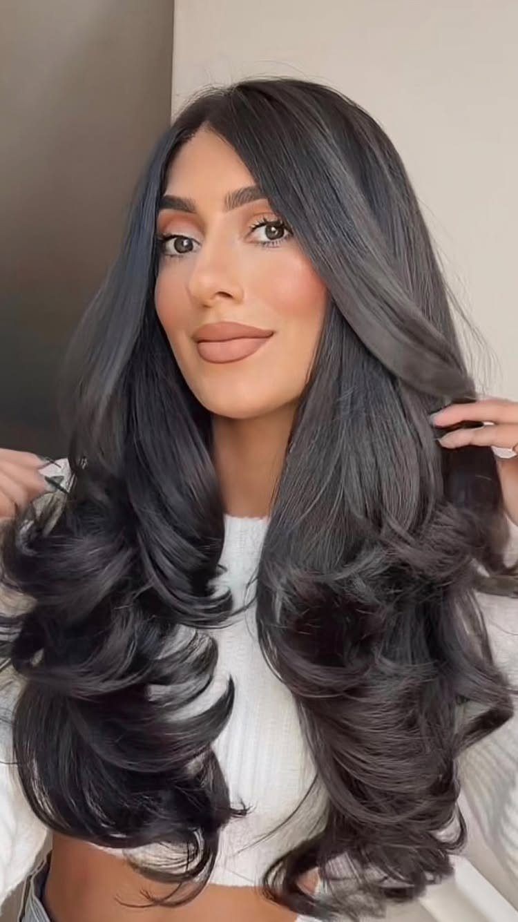 Woman with long dark hair styled in voluminous, swoopy curls and layers