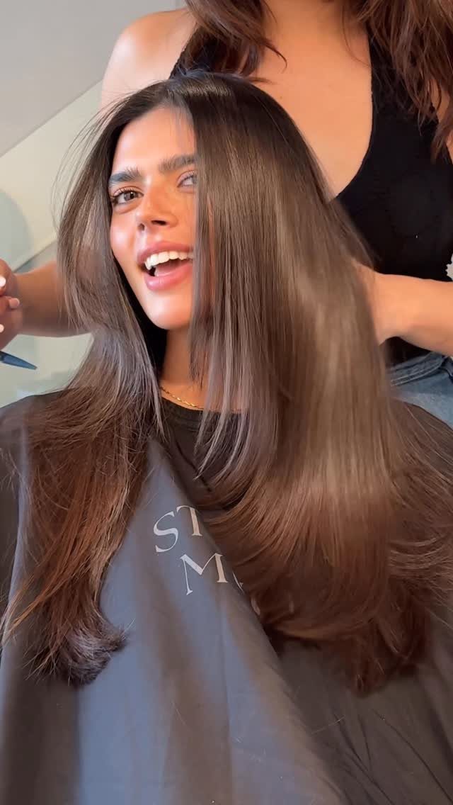 Long brown hair falls in smooth cascading layers over a salon cape