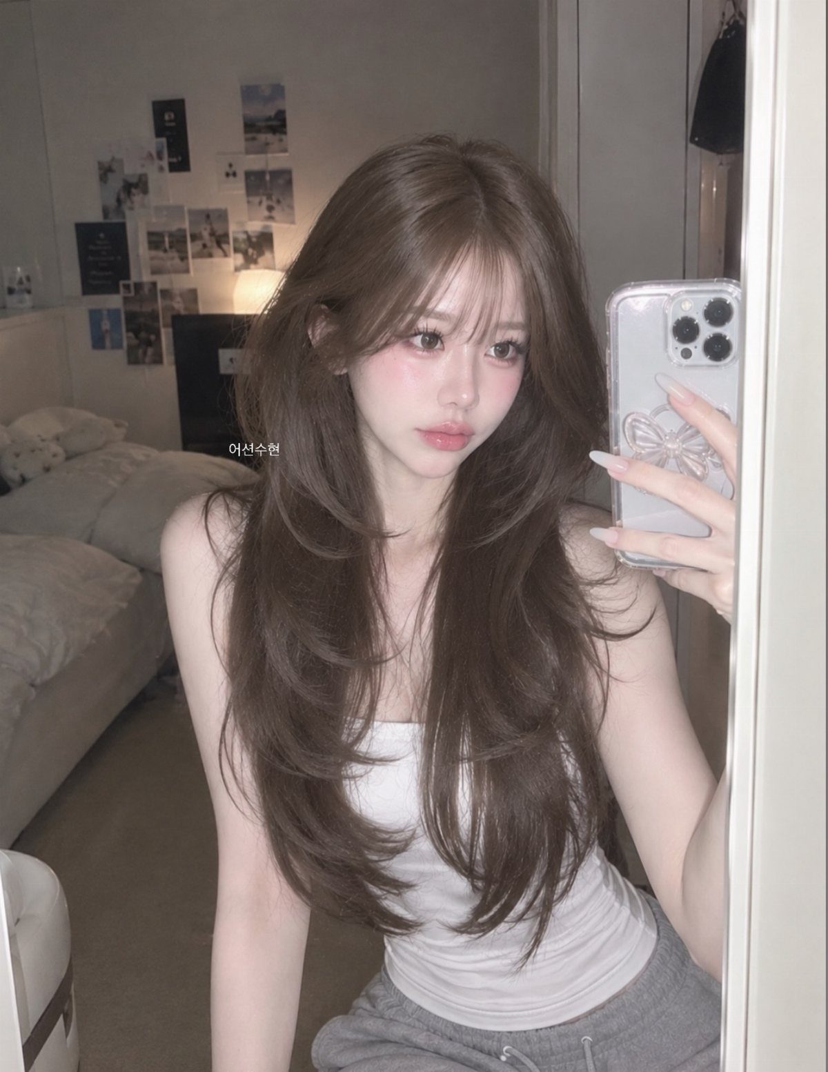 Woman with long brown hair, wispy bangs, and feather-light layers taking a mirror selfie