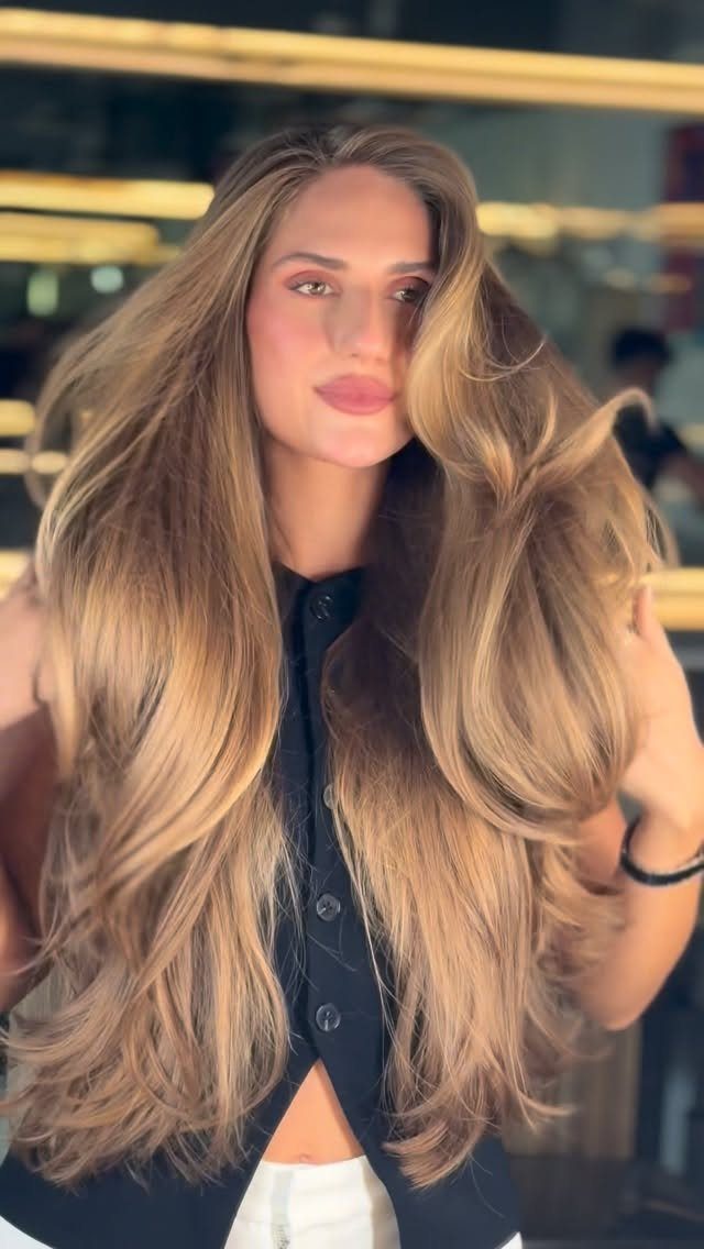 Woman with long blonde butterfly layers and outward-swept face-framing hair