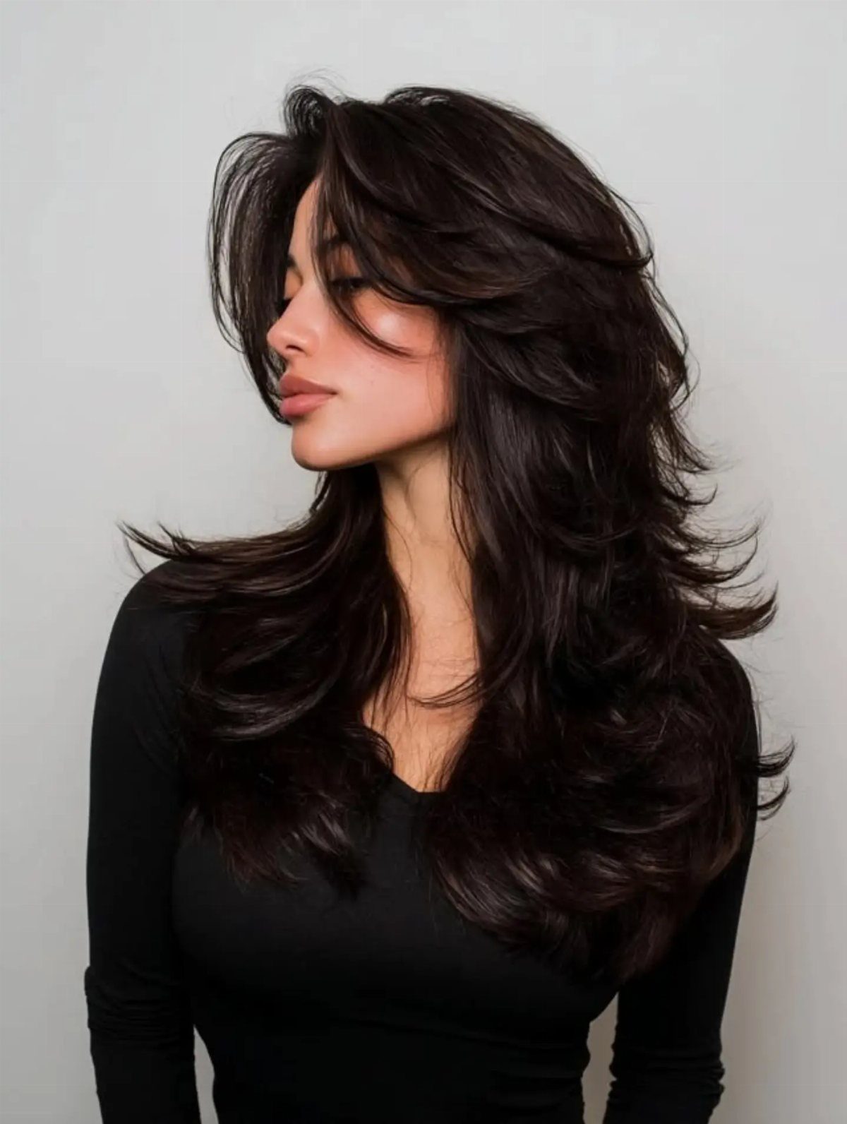 Woman with long dark cascading layers, curled ends, and a sweeping side fringe