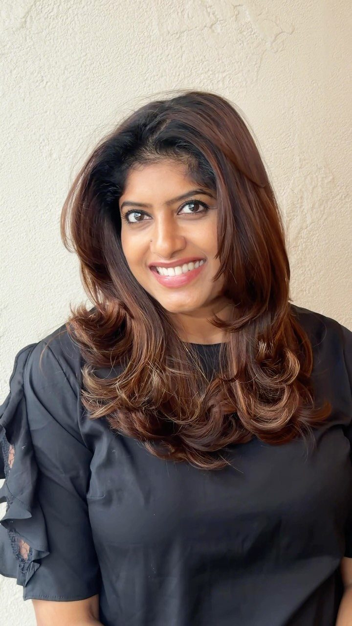 Woman wearing glossy chestnut brown long hair with face-framing layers and curled ends