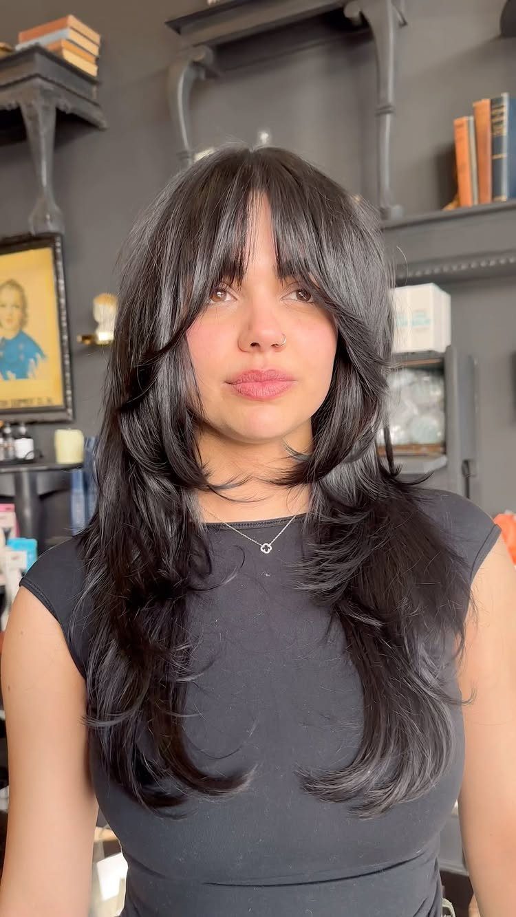 Woman with long dark layered hair and wispy bangs in a salon