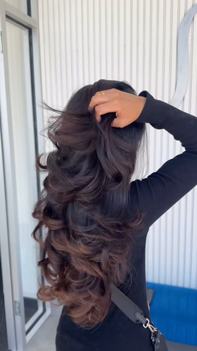 Long dark layered curls lifted by hand against a white paneled wall
