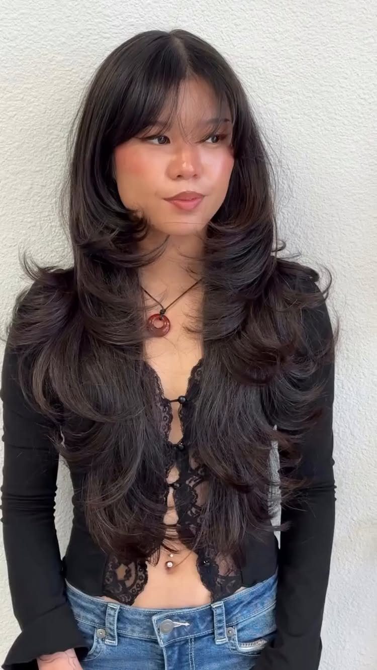 Woman with long dark hair, wispy bangs, and voluminous layered curls