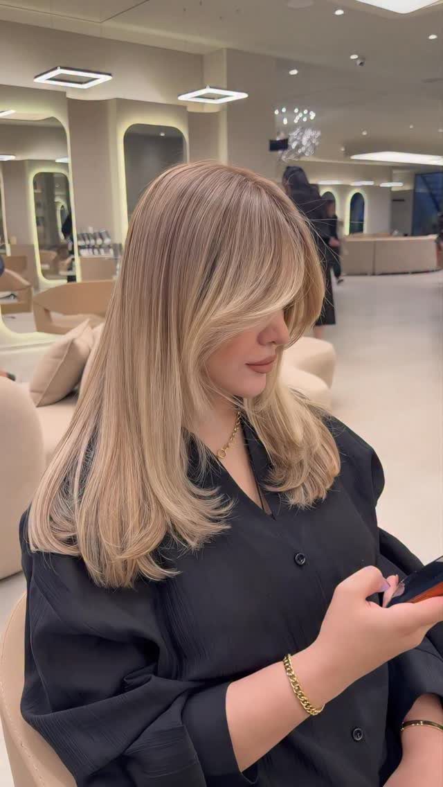 Woman with long sandy blonde balayage layers seated in a salon