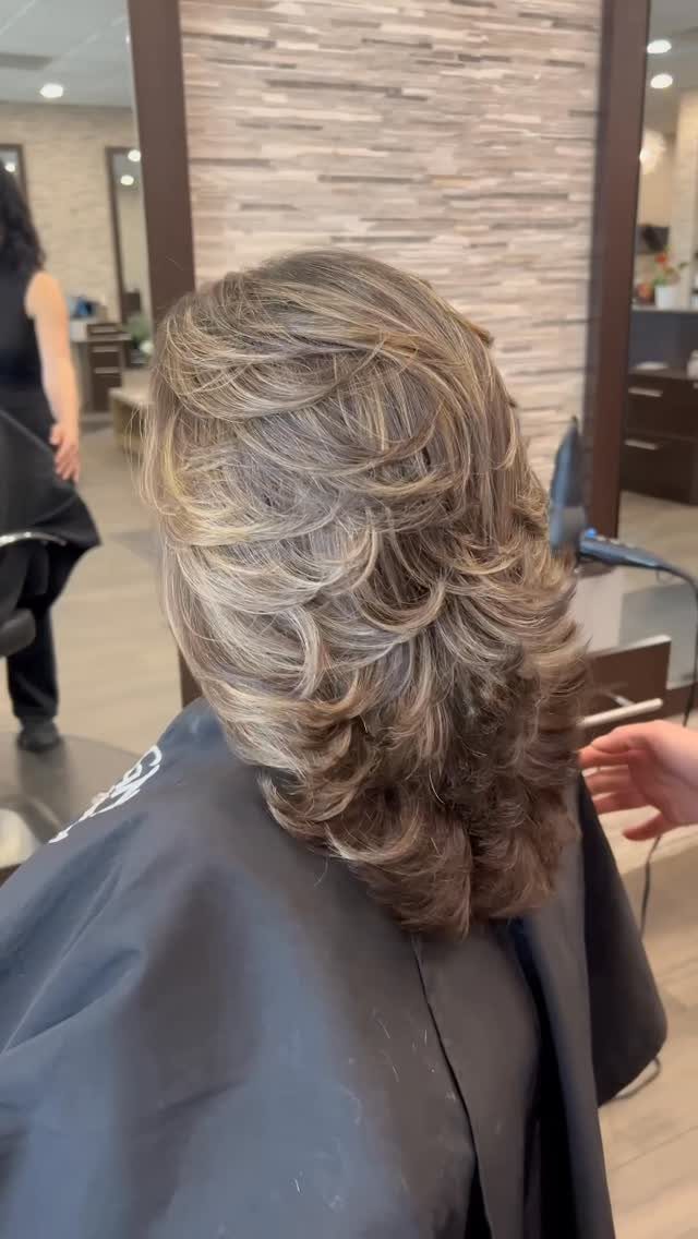 Voluminous ash-brown layered haircut with feathered, highlighted ends in a salon