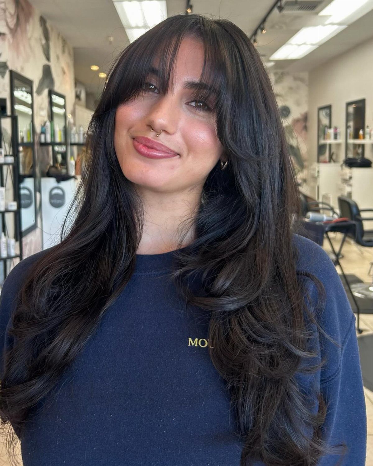 Woman showcasing long dark hair with soft wispy layers and curtain-like bangs in a salon