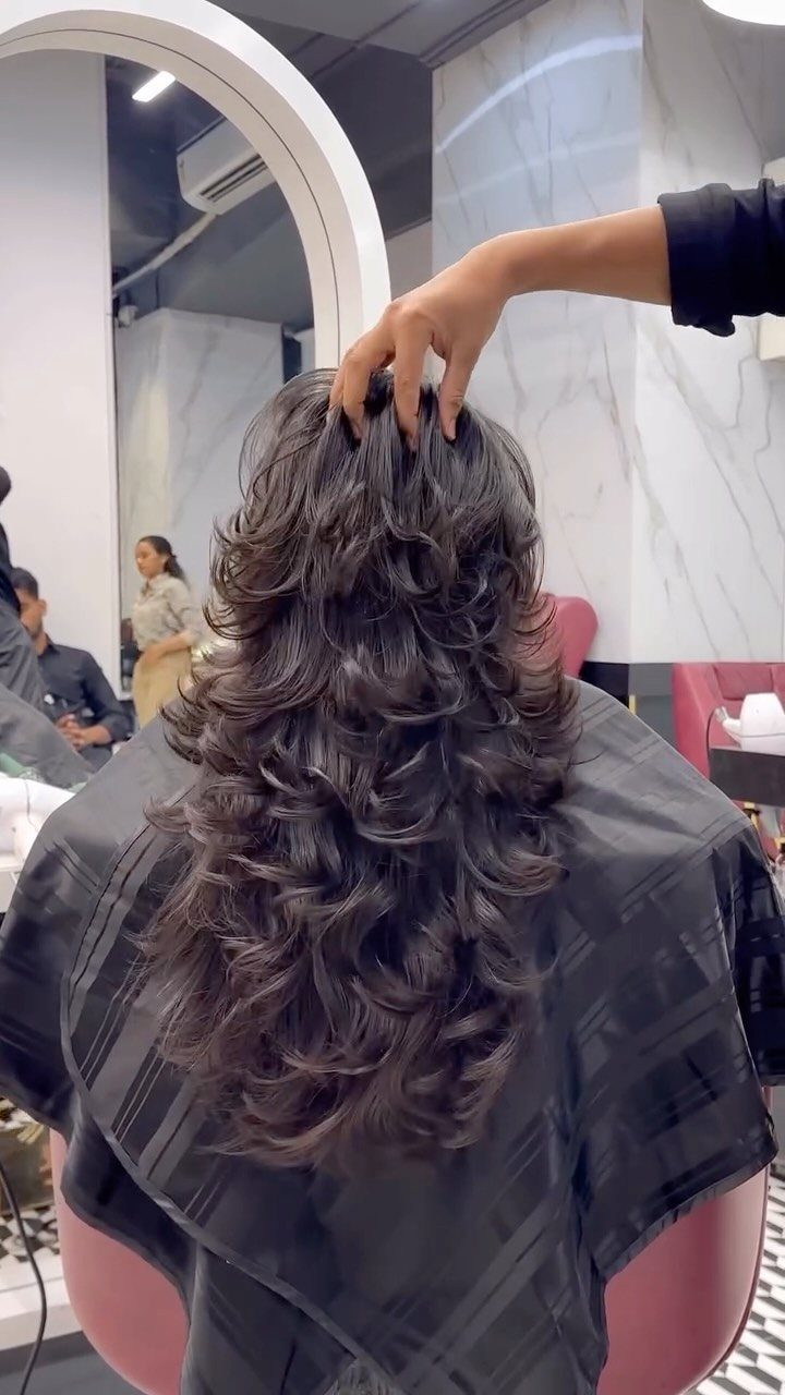 Layered dark curls cascade down a salon client's back beneath a stylist's hand