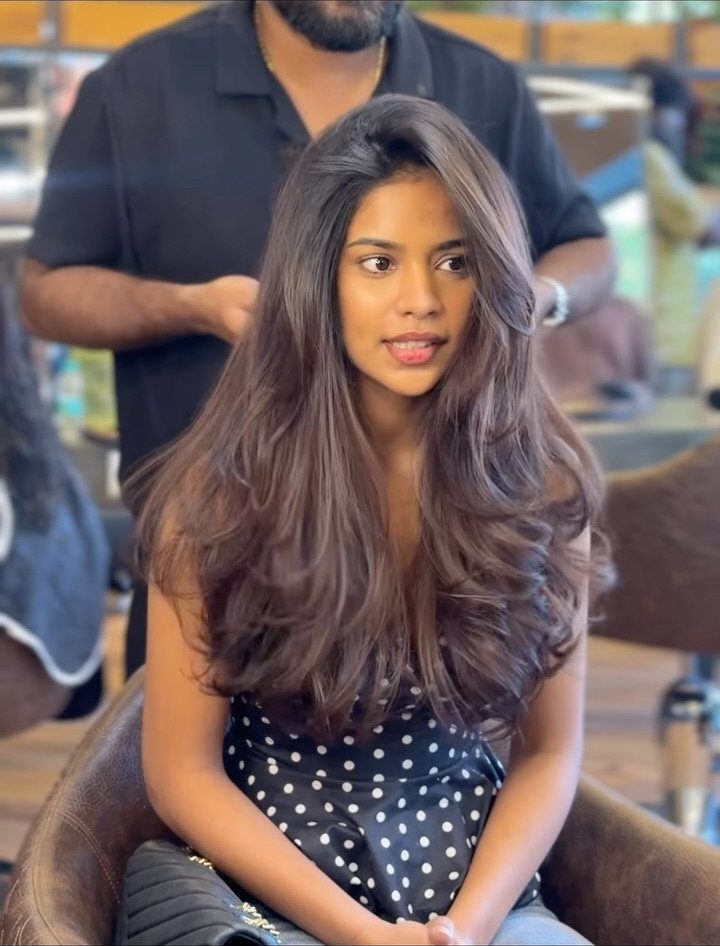 Woman with long, layered dark brown hair and curled ends sitting in a salon chair