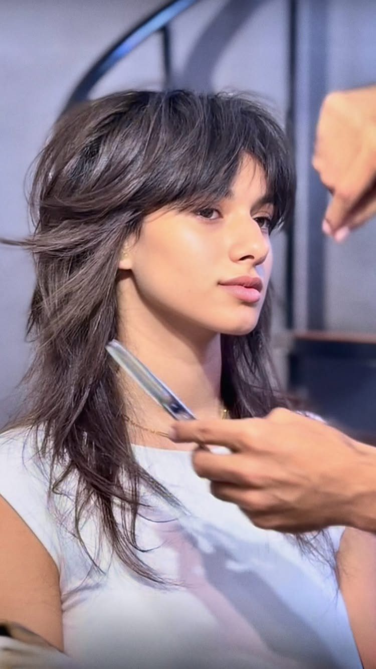 Woman with long dark layers and bangs sits as a stylist trims her hair