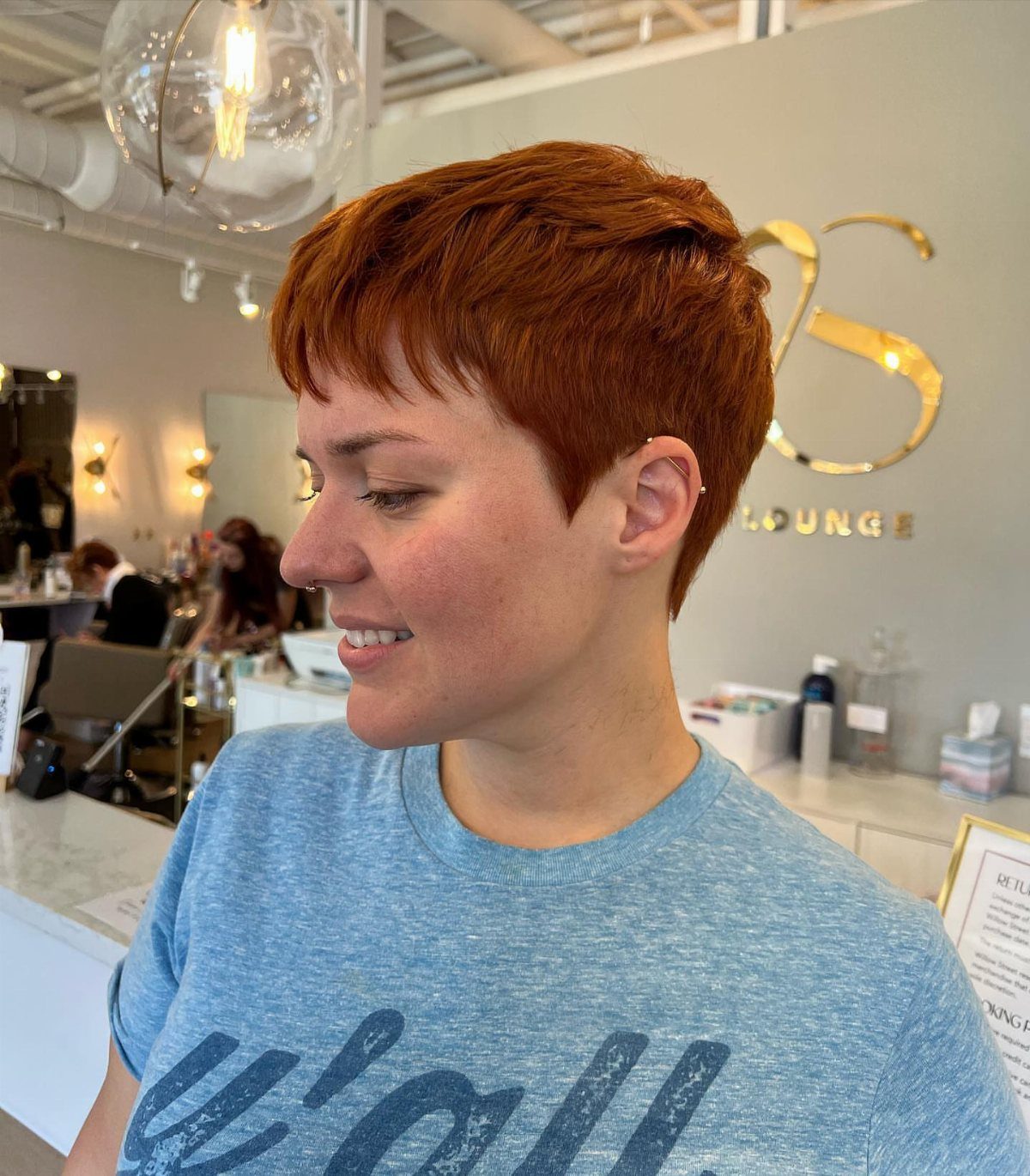 Copper-red pixie with short bangs shown in profile at a salon