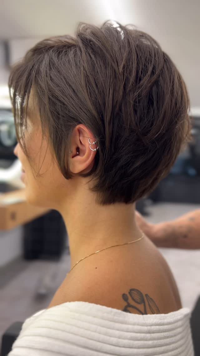 Side-profile person showing a dark choppy layered pixie haircut in a salon