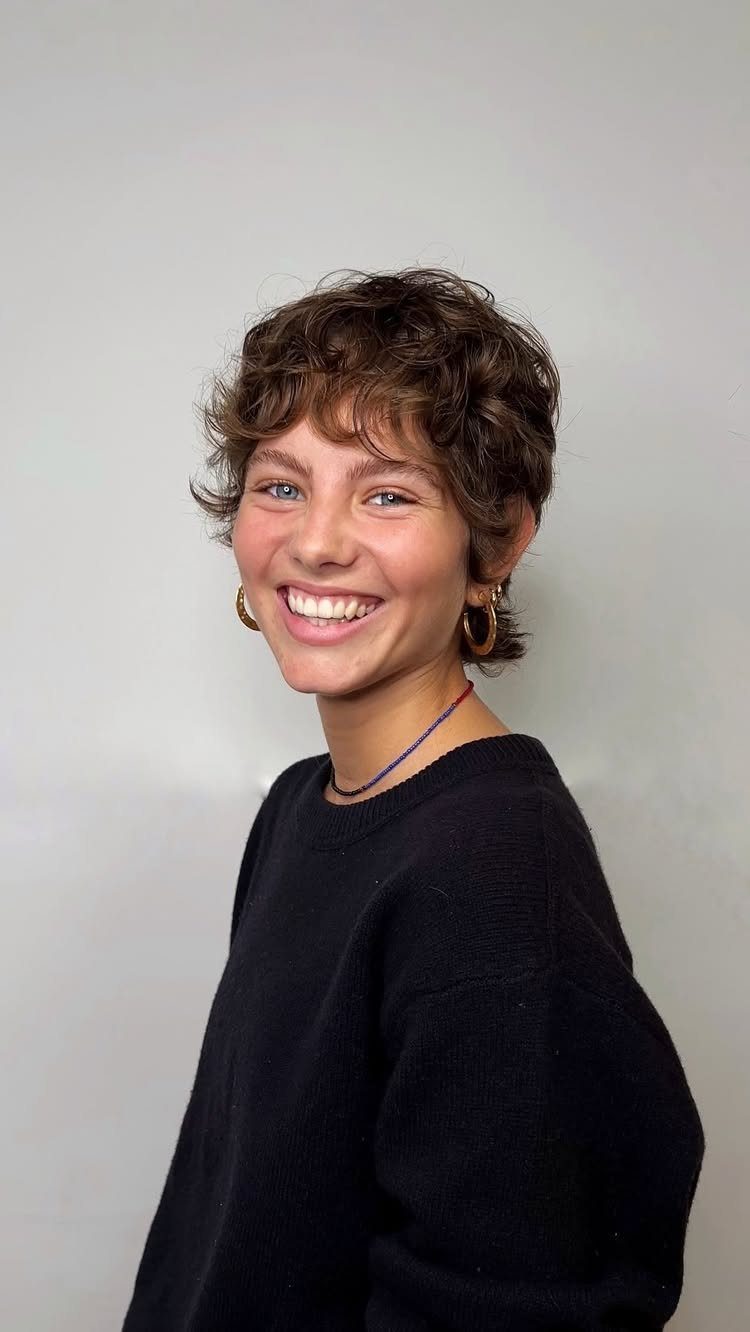 Person with short, naturally curly brown hair in a longer pixie cut