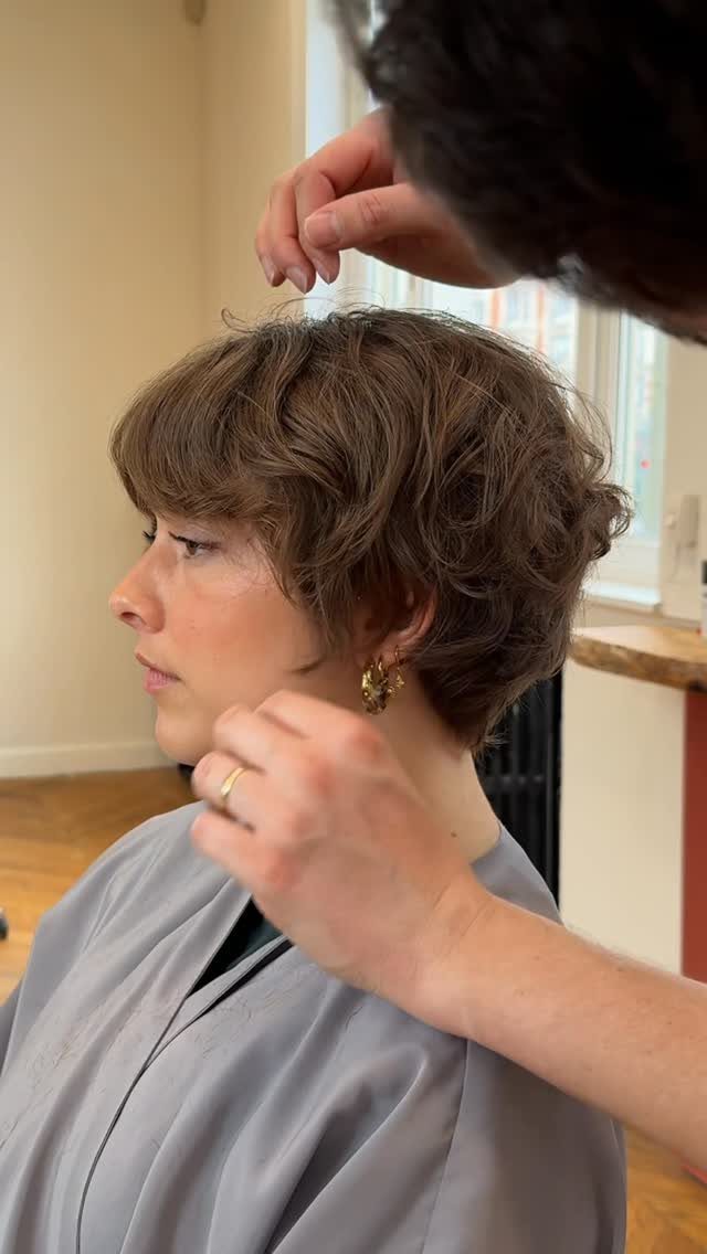 Woman with a layered long pixie cut having her hair adjusted in a salon