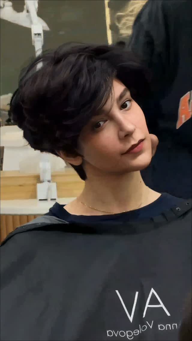 Person with a dark layered long pixie and side-swept face-framing bangs in a salon