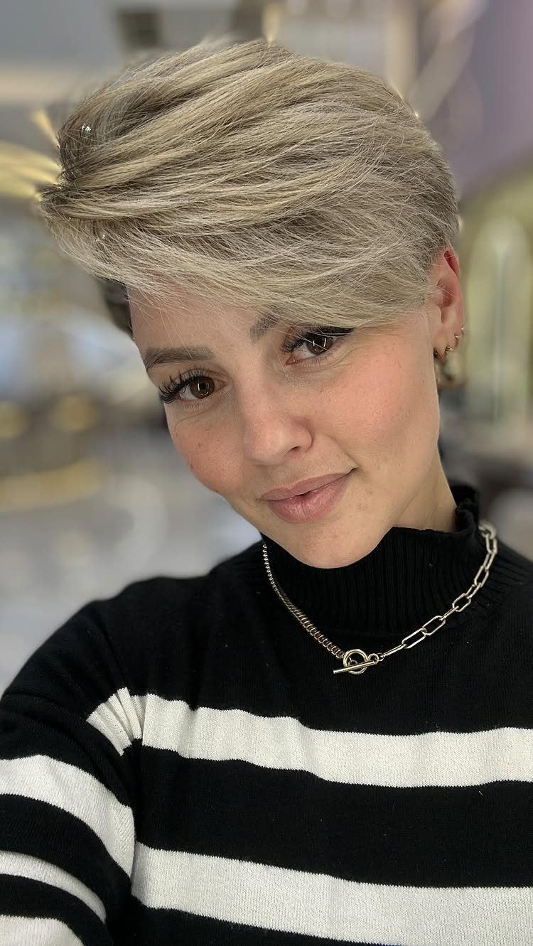 Person showing a blonde long pixie cut with full, side-swept bangs
