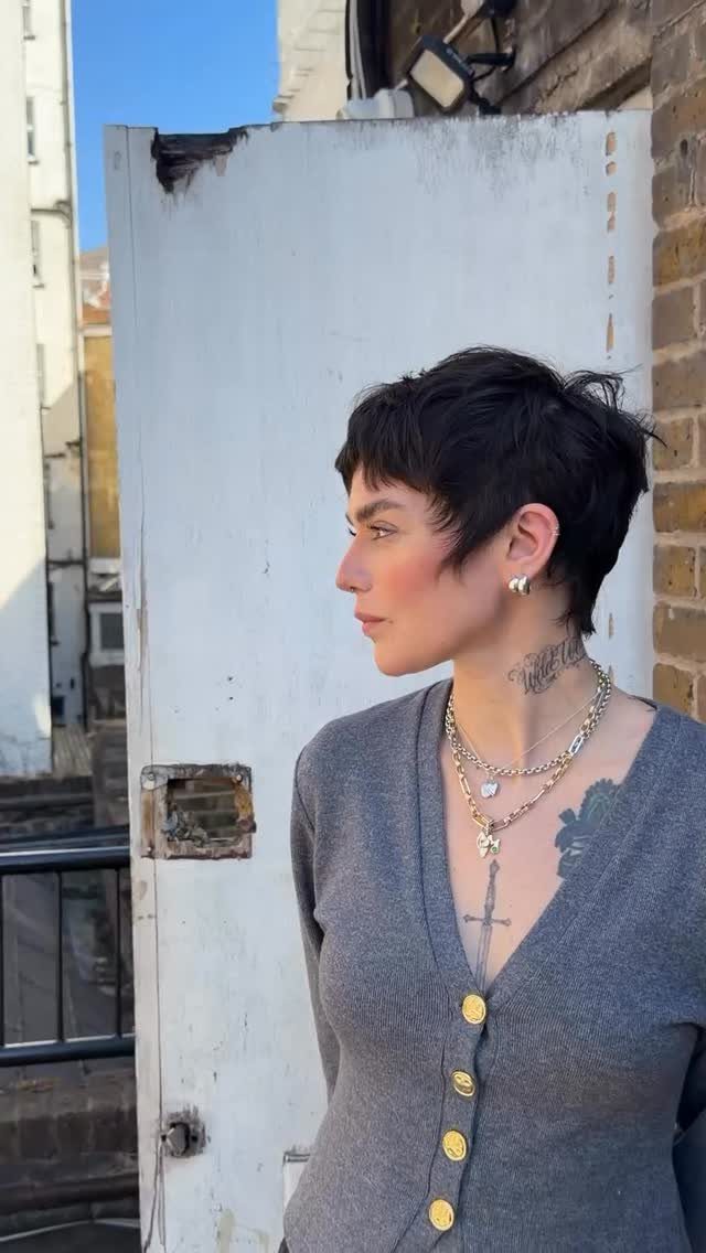 Side-profile person with dark textured long pixie haircut and angled fringe